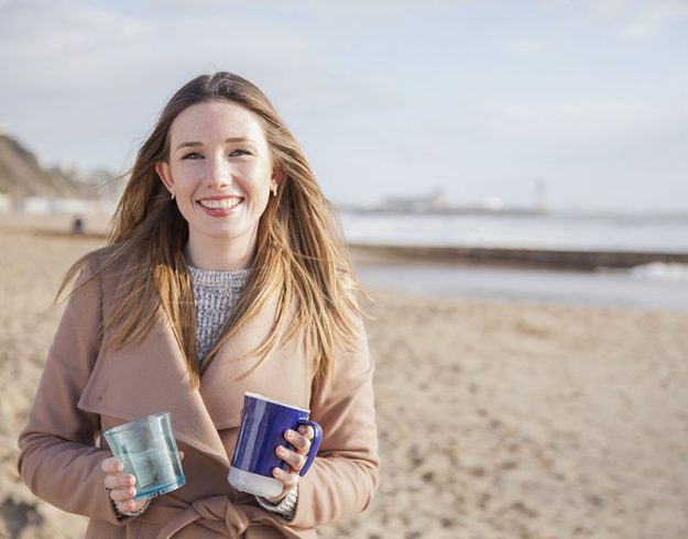 Ellie on a beach holding a Droplet-Reminder cup